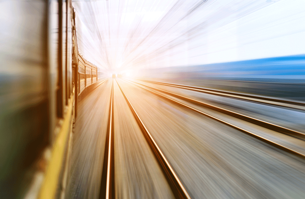 06 Train tracks leading towards the horizon with overhead wires and a train passing quickly.