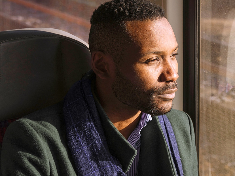 A person in a green coat and blue scarf sits by a train window.